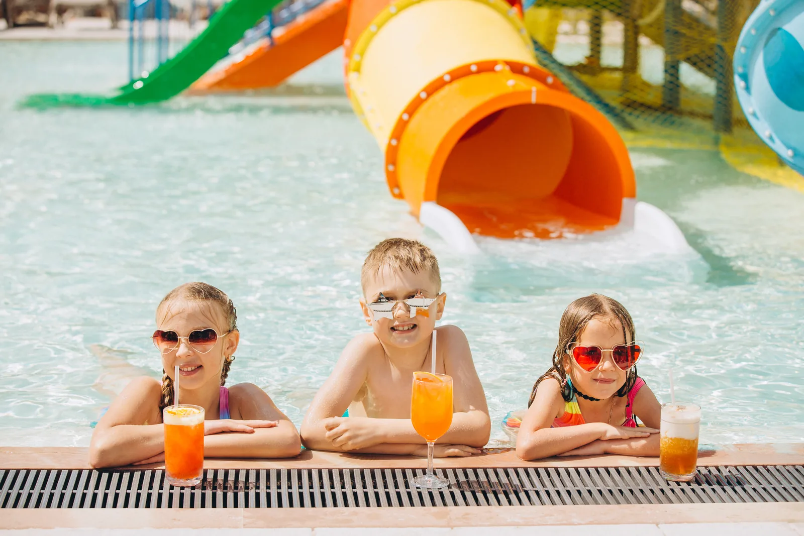 Children enjoying cold drinks beside a colorful water park